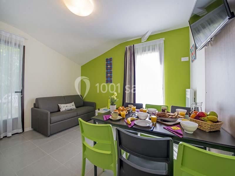 Salle à manger lumineuse avec table dressée pour le petit-déjeuner, canapé gris et murs verts.