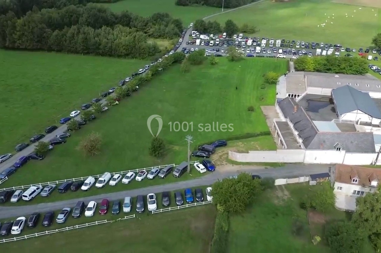 Vue aérienne d'un parking bondé entourant un bâtiment dans une zone rurale avec des champs et des arbres.