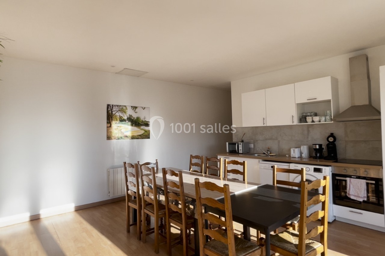 Salle à manger lumineuse avec une grande table en bois, des chaises assorties et une cuisine ouverte équipée en arrière-plan.