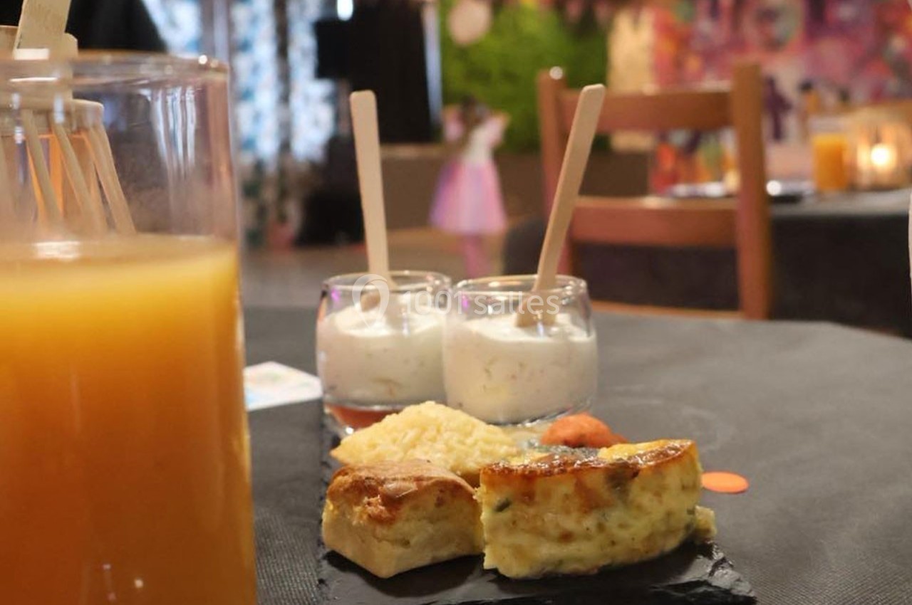 Assiette avec quiche, riz et saumon, accompagnée de verrines et d'un verre de jus sur une table dressée.