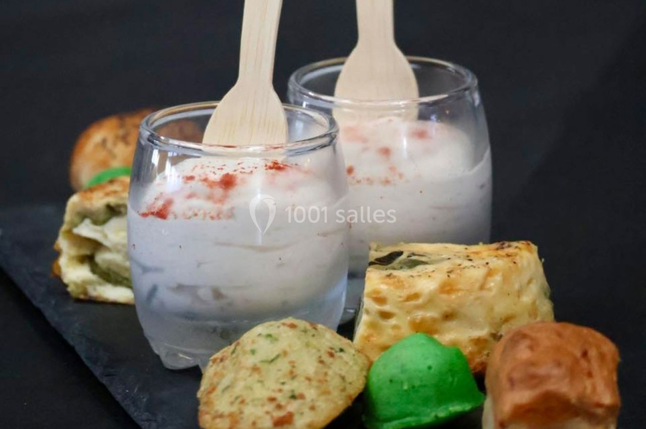Deux verrines de mousse blanche avec cuillères en bois, accompagnées de petits pains variés sur une ardoise noire.