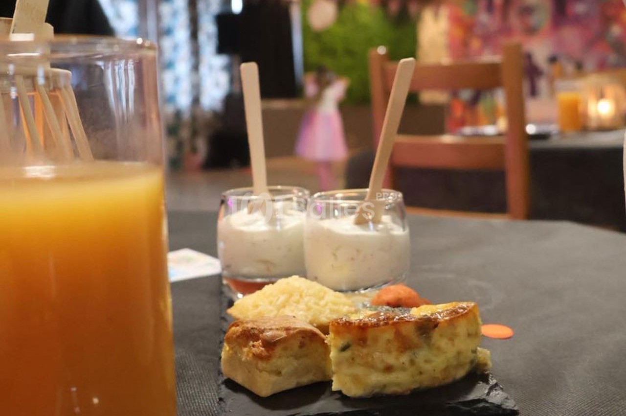 Assiette avec quiche, riz et verrines de dessert sur une table noire, avec un verre de jus d'orange au premier plan.
