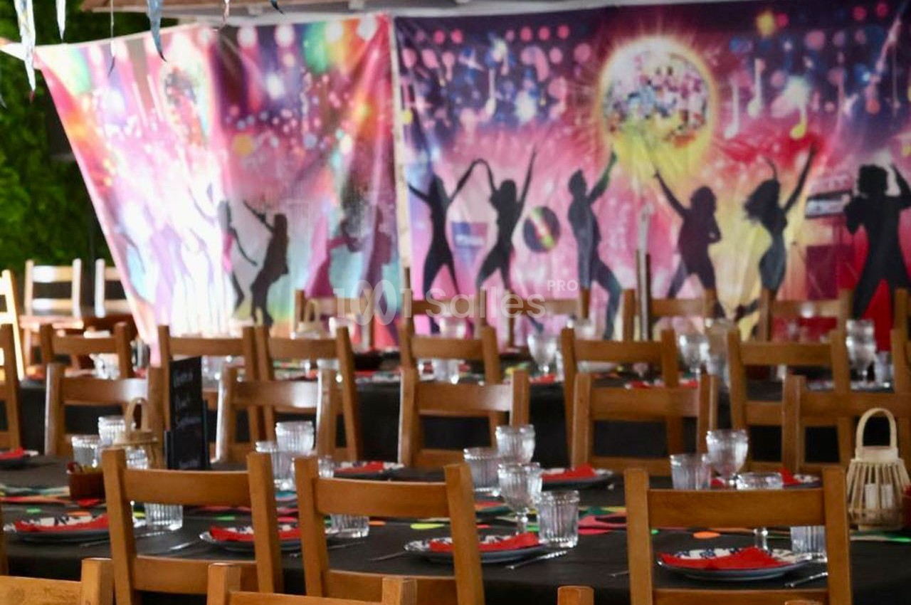 Salle décorée pour un événement festif, avec tables dressées et fond coloré représentant des silhouettes dansantes.