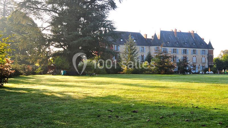 Grand bâtiment historique entouré d'un vaste jardin verdoyant avec des arbres et une pelouse ensoleillée.