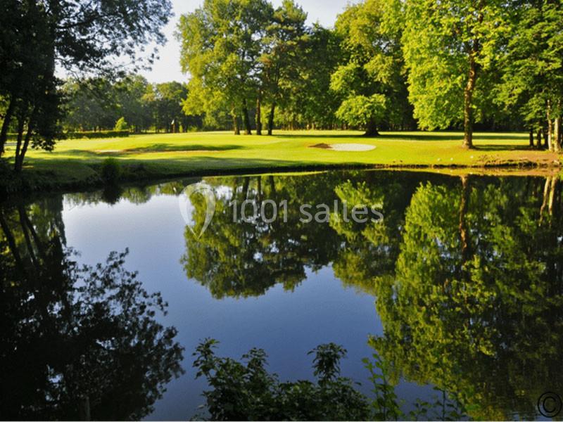 Étang calme reflétant des arbres et une pelouse verdoyante avec un bunker de golf en arrière-plan.