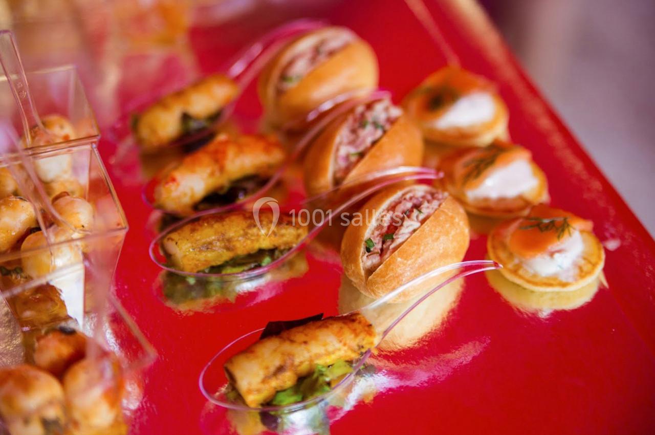 Assortiment de bouchées apéritives variées présentées sur une table rouge, incluant mini-sandwichs et verrines.