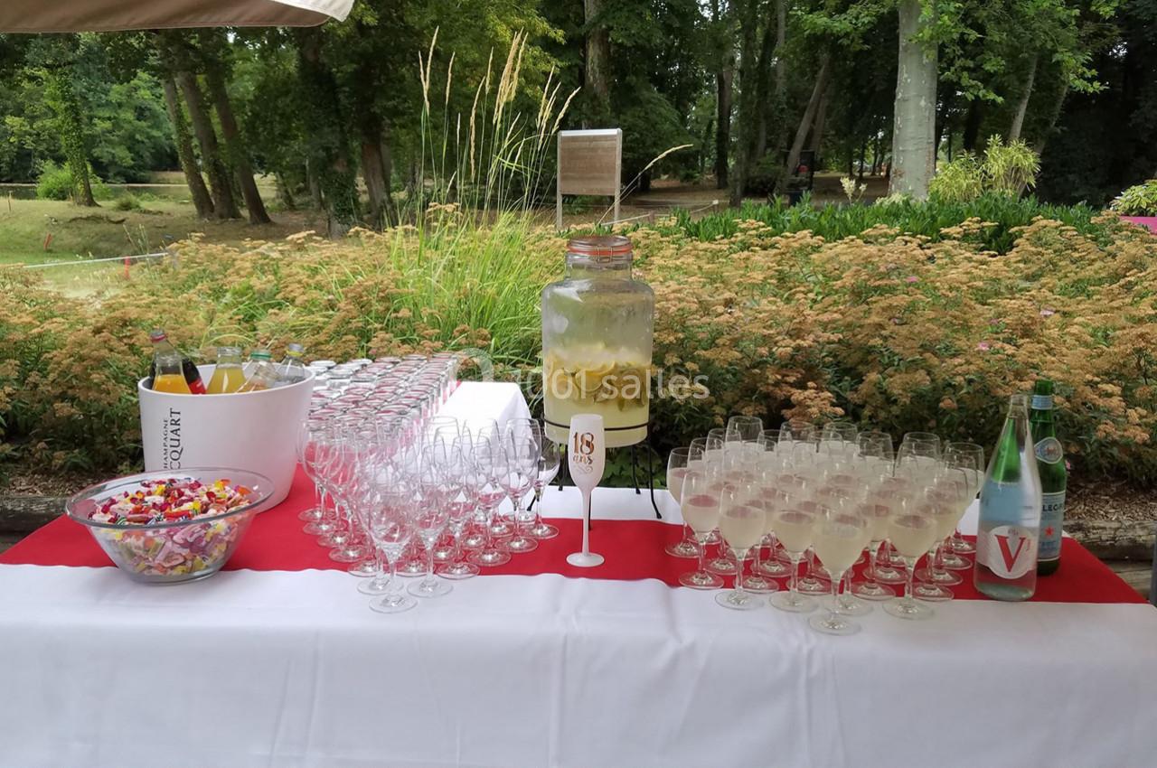 Table dressée en extérieur avec des verres, une jarre de citronnade, des bonbons et des bouteilles d'eau.