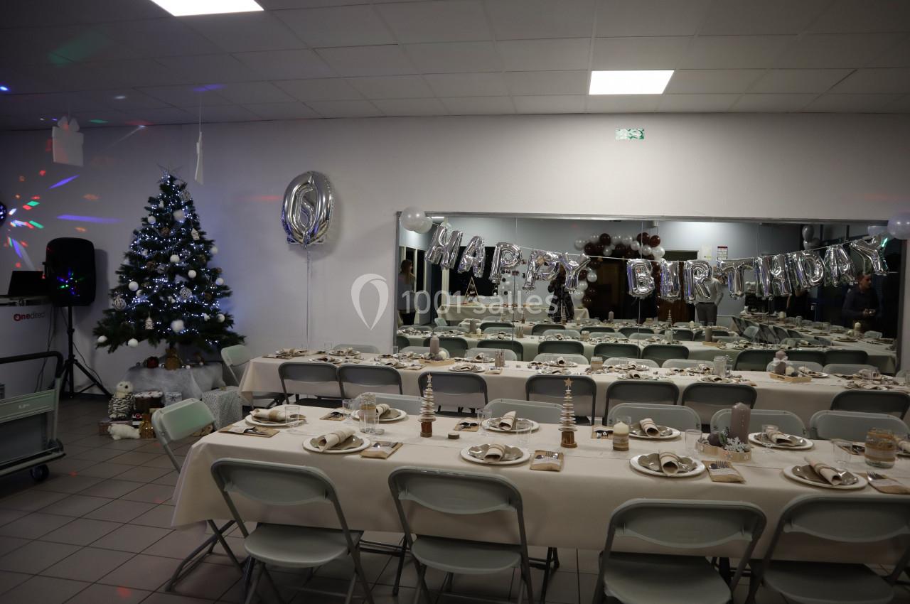 Salle décorée pour un anniversaire avec tables dressées, guirlande ’Happy Birthday’ et sapin illuminé.