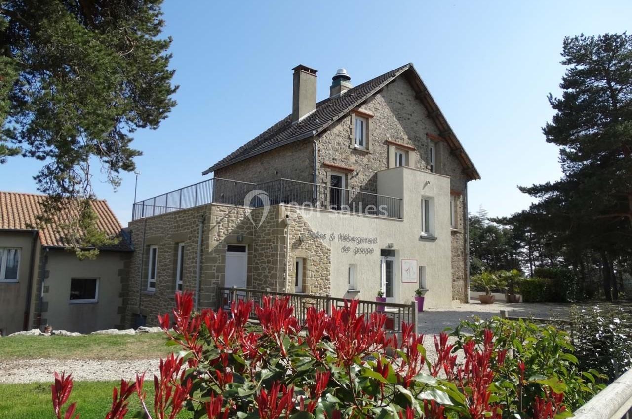 Grande maison en pierre avec terrasse, entourée de végétation et située dans un environnement rural.