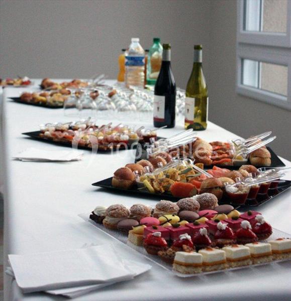 Buffet avec plateaux de viennoiseries, desserts, amuse-bouches, bouteilles de vin et boissons disposés sur une table blanche.