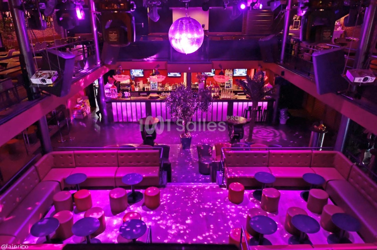 Vue intérieure d'une discothèque avec une piste de danse, des banquettes, un bar illuminé et une boule à facettes au plafond.