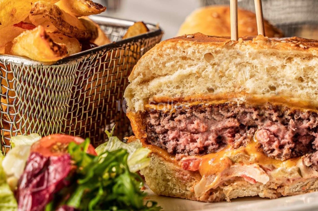 Burger coupé en deux montrant une viande juteuse, fromage fondu, légumes, accompagné de frites et salade.