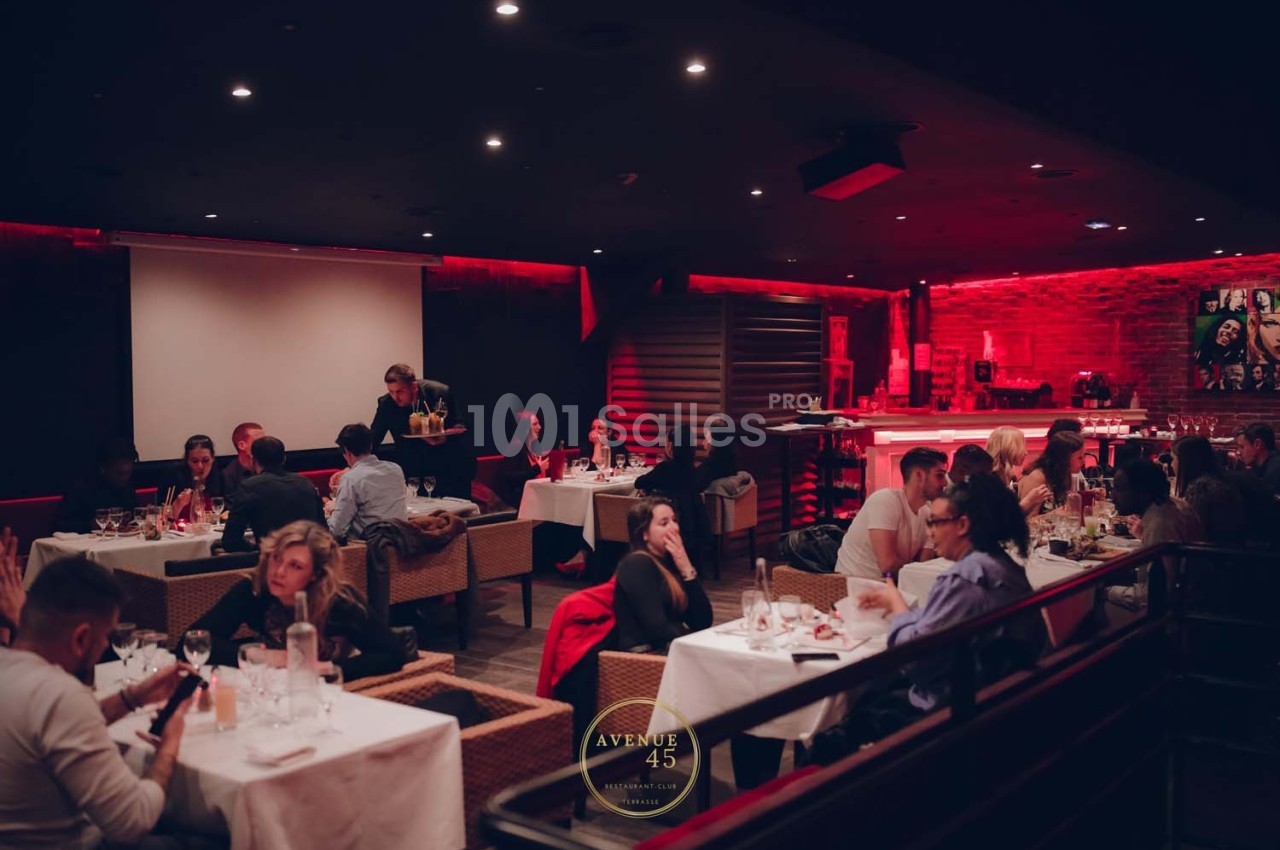 Salle de restaurant animée avec des tables occupées, éclairage tamisé et décor chaleureux.