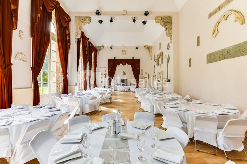 Salle de réception lumineuse avec tables rondes dressées de nappes blanches, entourée de rideaux rouges et décorations…