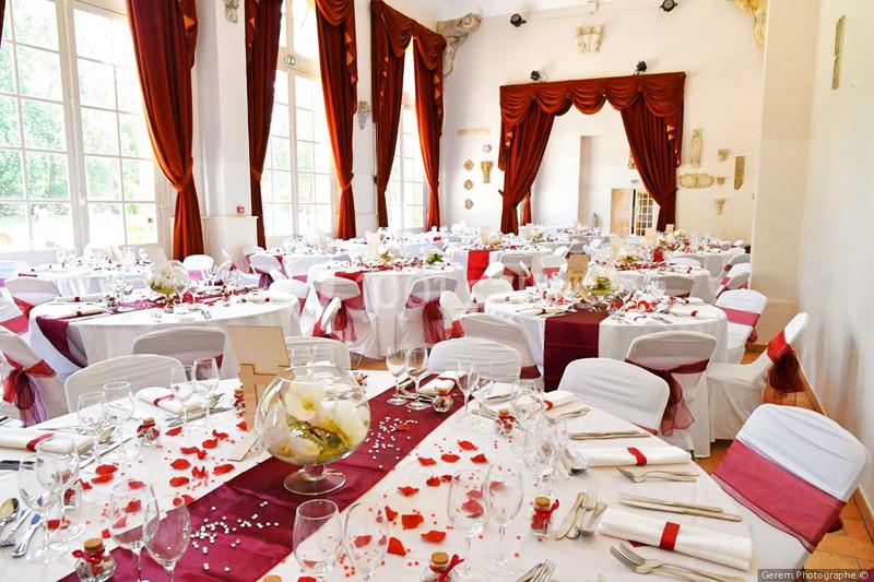 Salle de réception élégante décorée avec des nappes blanches et rouges, tables dressées pour un événement festif.