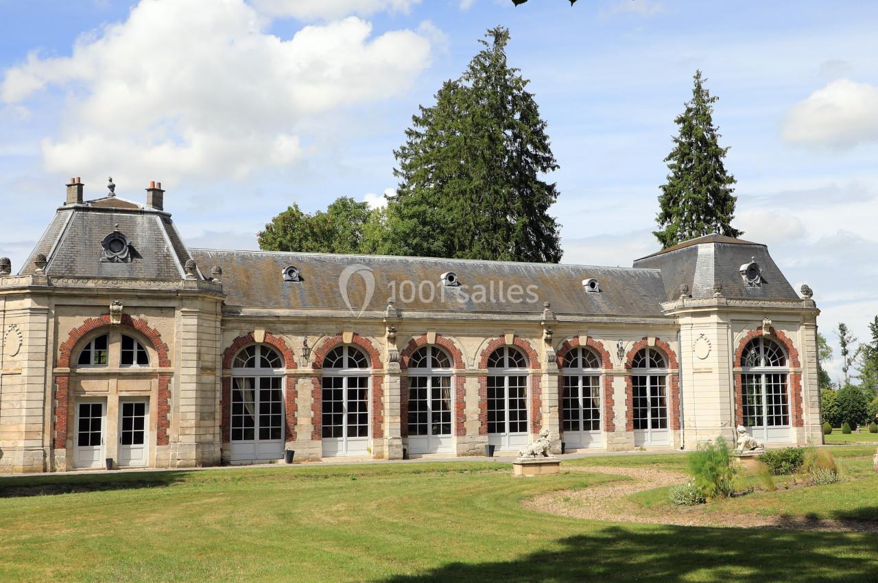Bâtiment ancien en pierre et briques avec grandes fenêtres cintrées, entouré de pelouse et d'arbres.