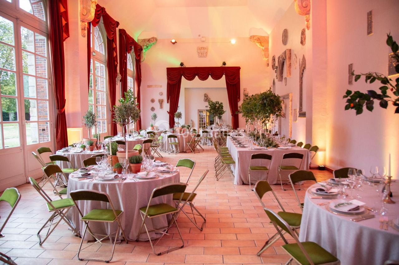 Salle de réception élégante avec tables rondes dressées, chaises pliantes vertes et décoration végétale.