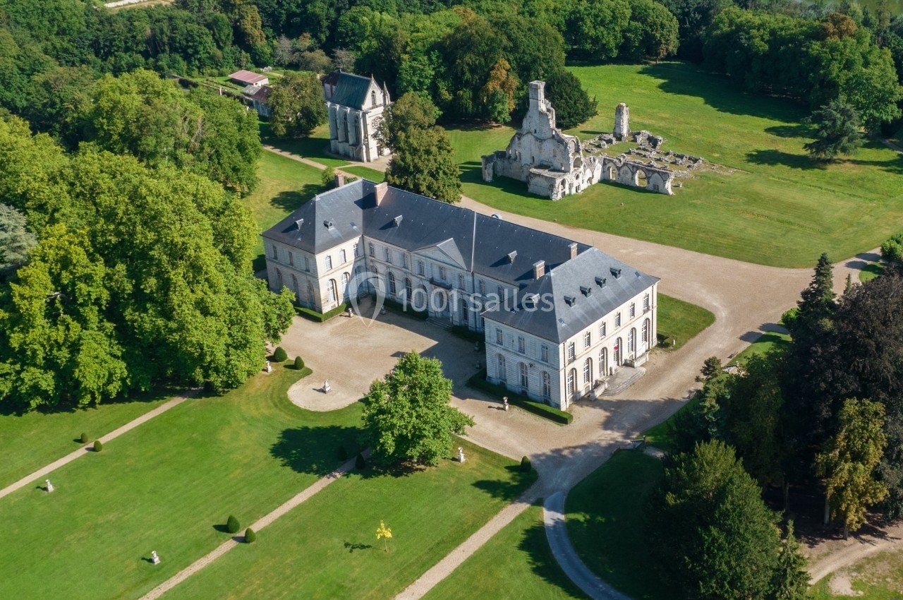Vue aérienne d'un château entouré de jardins verdoyants et de ruines historiques dans un cadre arboré.