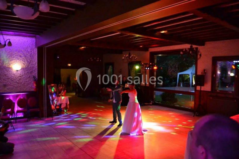 Un couple danse au centre d'une salle éclairée par des lumières colorées, entouré de quelques invités.