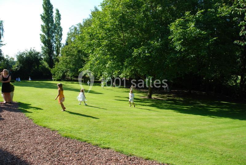 Des enfants jouent sur une pelouse ensoleillée entourée d'arbres dans un parc spacieux.