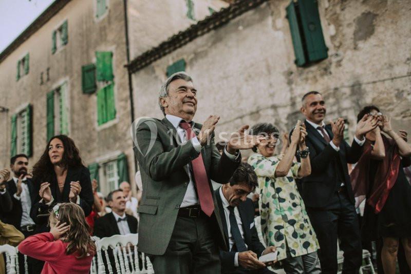 Des personnes applaudissent debout lors d'un événement en extérieur devant un bâtiment ancien.