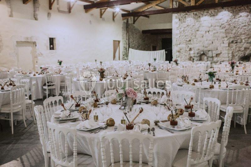 Salle de réception décorée avec des tables rondes dressées, nappes blanches et chaises assorties, ambiance élégante.
