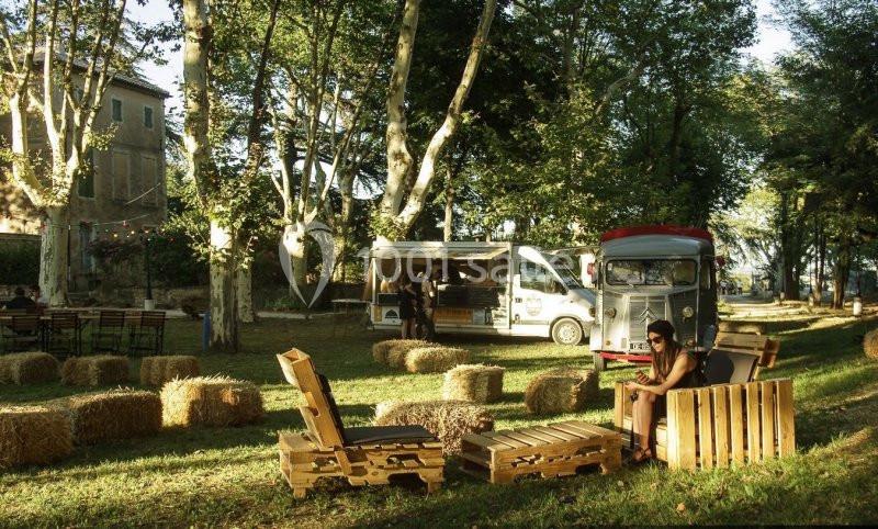 Un espace extérieur avec des palettes en bois aménagées en sièges, des bottes de paille et des food trucks sous des arbres.