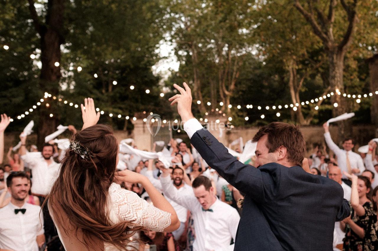 Un couple danse lors d'une fête en plein air, entouré d'invités joyeux sous des guirlandes lumineuses.