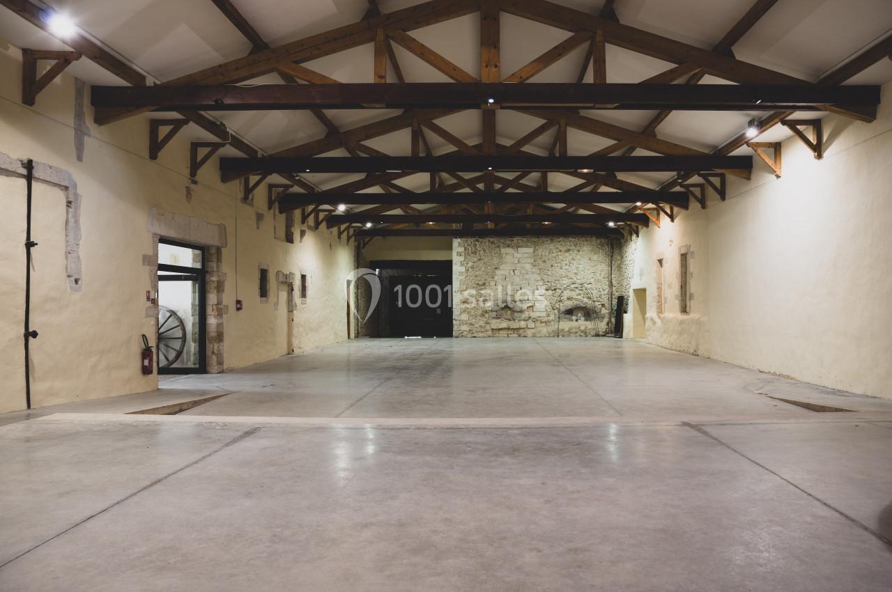 Intérieur d'une grande salle vide avec plafond en poutres apparentes et murs en pierre et plâtre.