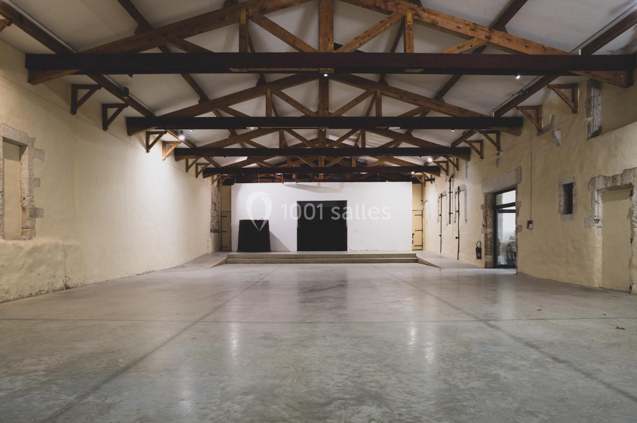 Intérieur d'un grand espace vide avec plafond en poutres apparentes et murs en pierre claire.