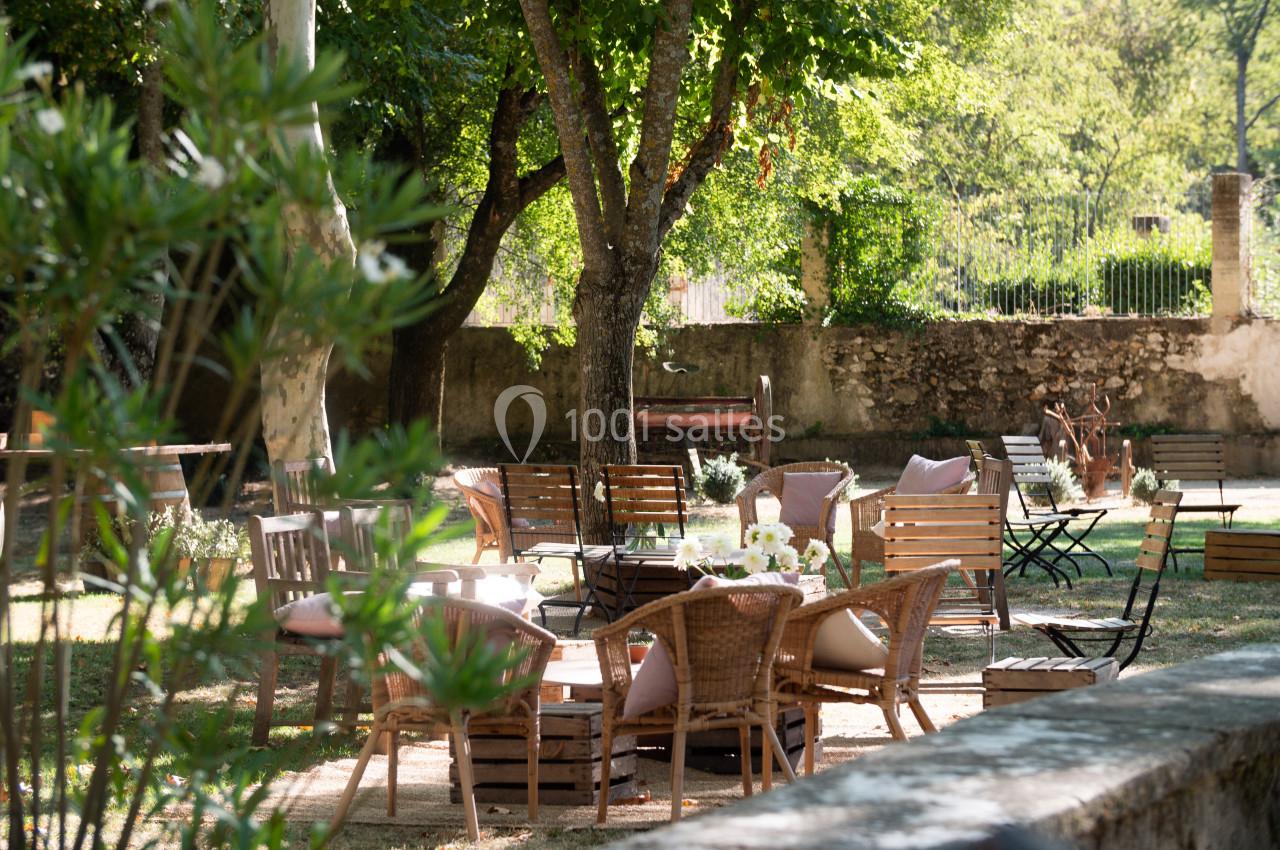 Mobilier de jardin en bois et rotin disposé sous des arbres dans un espace extérieur ombragé.