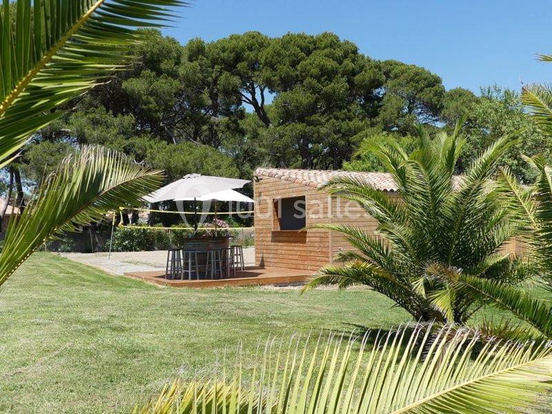 Abri en bois avec terrasse et parasol dans un jardin verdoyant entouré de palmiers et d'arbres.