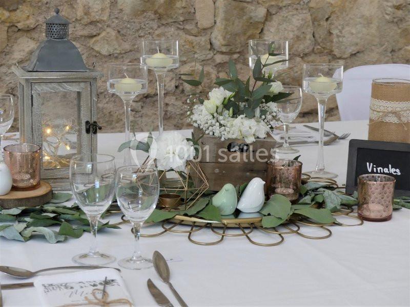 Table décorée pour un événement avec bougies, fleurs blanches, lanternes et éléments rustiques sur une nappe blanche.
