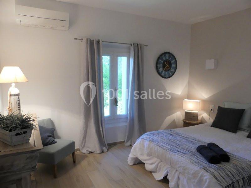 Chambre lumineuse avec lit double, lampes de chevet, fenêtre avec rideaux clairs et décoration sobre.