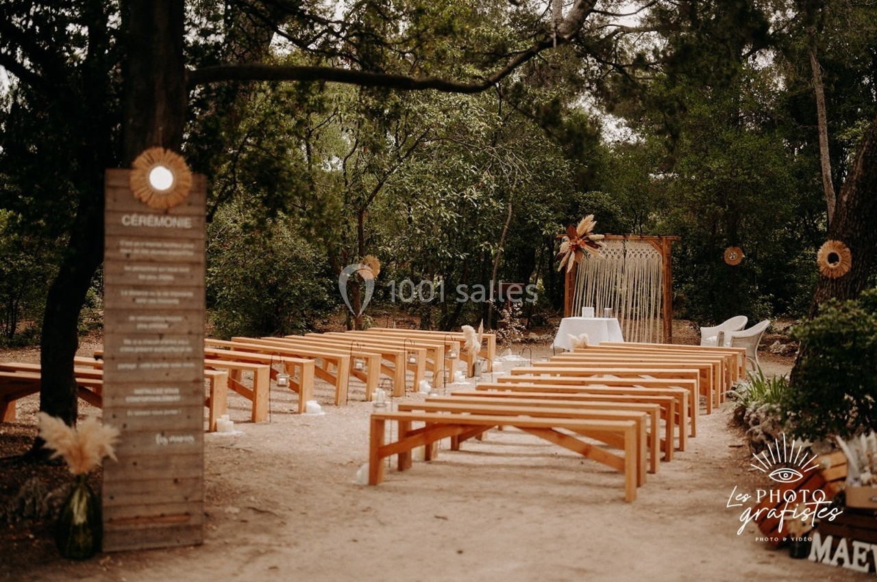Disposition de bancs en bois dans une clairière forestière, avec une arche décorée pour une cérémonie en plein air.