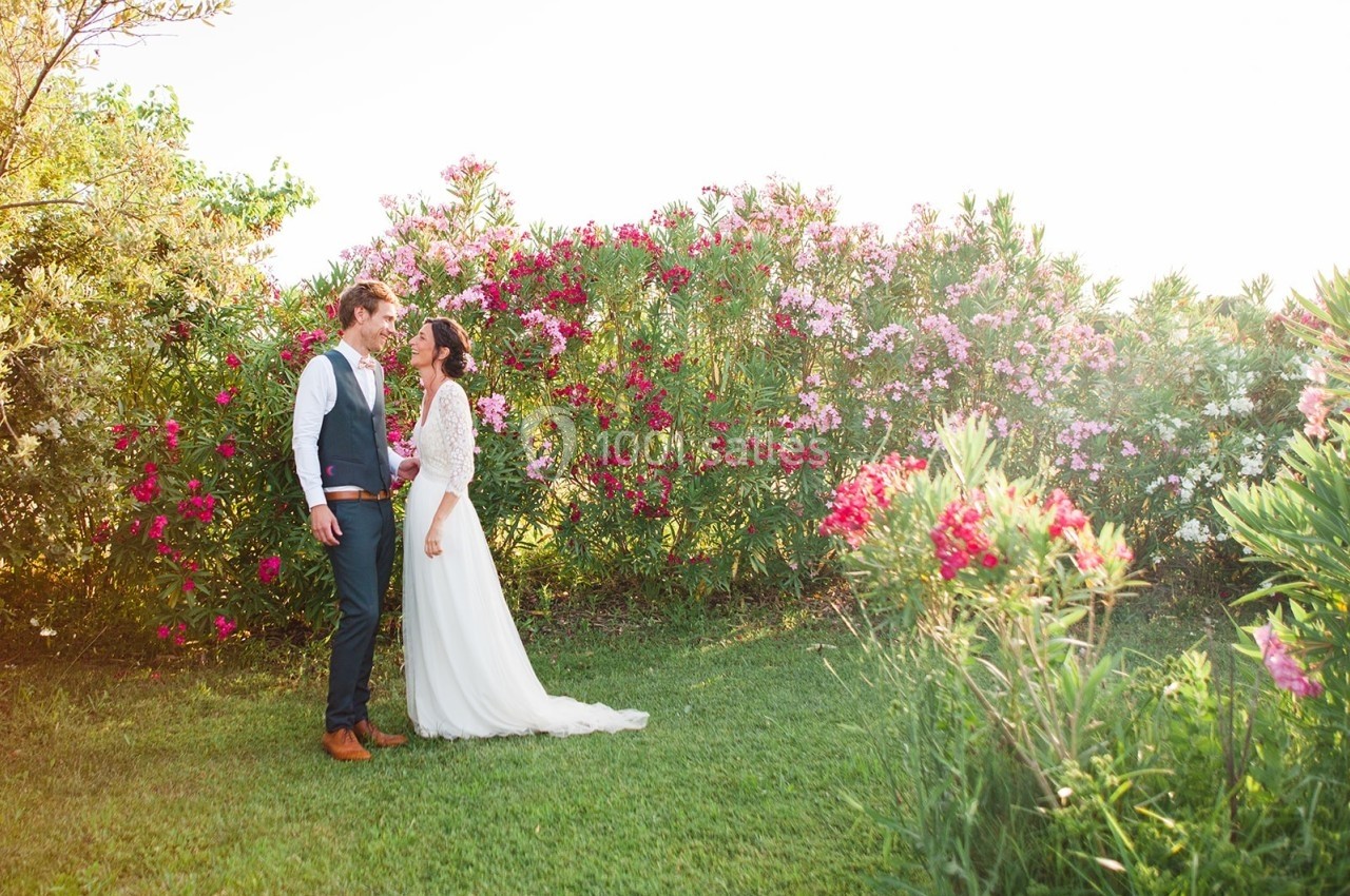 Un couple en tenue de mariage se tient debout dans un jardin fleuri sous une lumière naturelle.