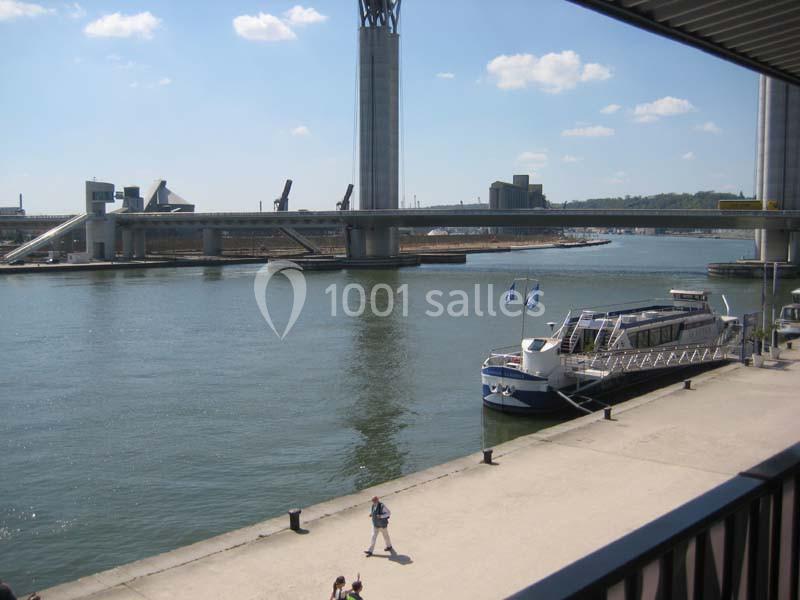Vue d'un quai avec un bateau amarré, une rivière, un pont moderne et des bâtiments industriels en arrière-plan.