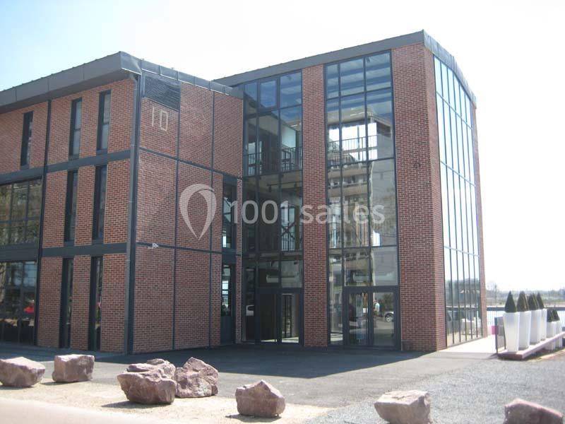 Bâtiment moderne en briques rouges avec de grandes façades vitrées, entouré de pierres décoratives au sol.