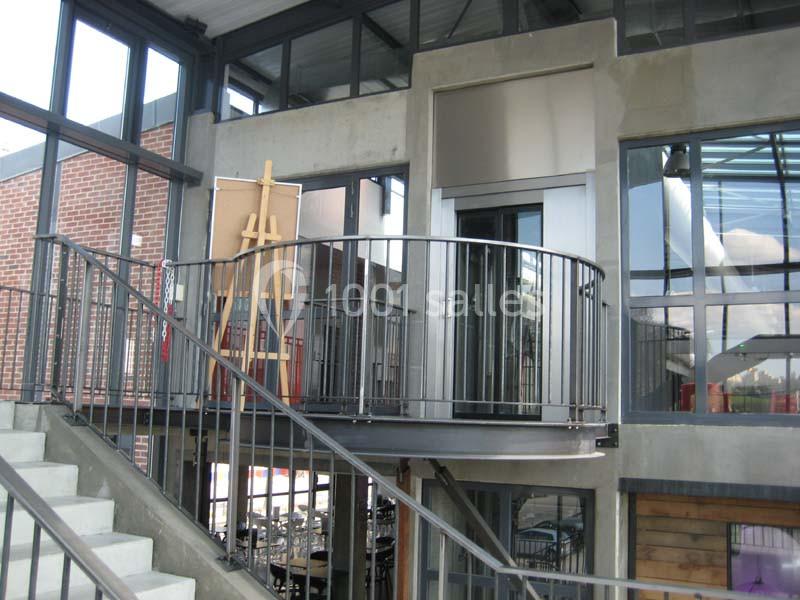 Escalier intérieur en métal avec une plateforme accessible par un ascenseur, entouré de grandes fenêtres.