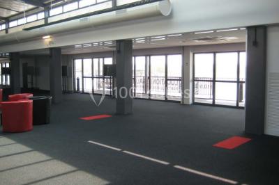 Miniature Location salle Rouen (Seine-Maritime) - Vue Sur Seine #9 Espace intérieur lumineux avec fauteuils rouges et noirs, tables hautes, plantes et stands d'exposition en arrière-plan.