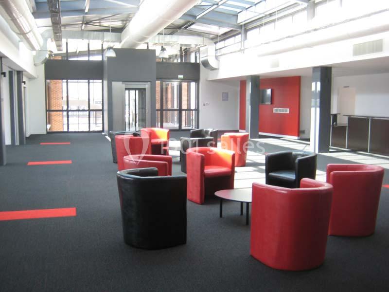 Espace intérieur lumineux avec fauteuils rouges et noirs disposés autour de petites tables, sol en moquette sombre.