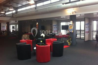 Miniature Location salle Rouen (Seine-Maritime) - Vue Sur Seine #14 Espace intérieur lumineux avec fauteuils rouges et noirs, tables hautes, plantes et stands d'exposition en arrière-plan.