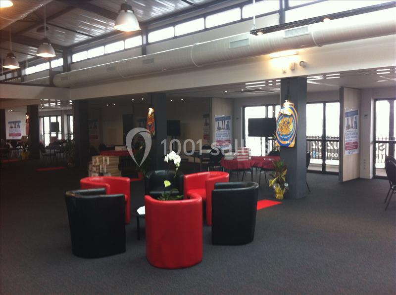 Salle lumineuse avec fauteuils rouges et noirs disposés autour de tables, entourée de grandes baies vitrées.