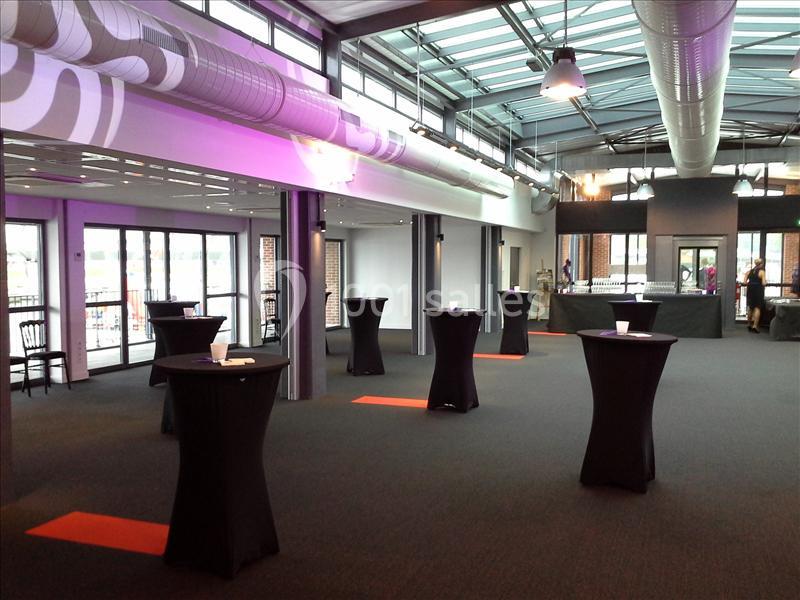 Salle moderne avec tables hautes noires, grandes baies vitrées et éclairage industriel.