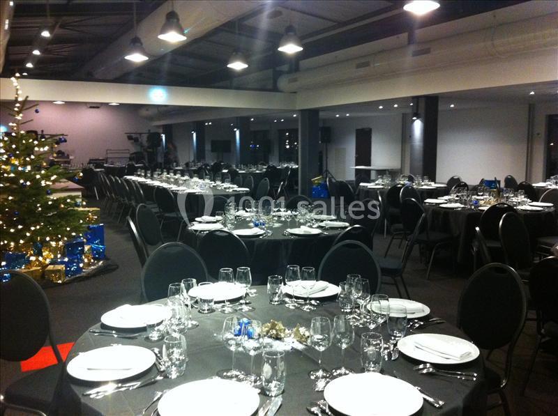 Salle de réception décorée avec des tables rondes dressées, éclairage tamisé et sapin de Noël illuminé.