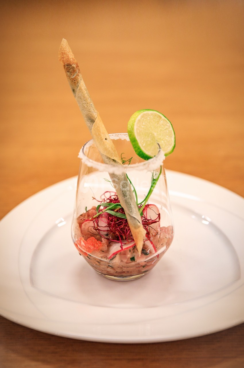 Verrine de tartare garnie d'une rondelle de citron, d'herbes fraîches et d'un bâtonnet croustillant.