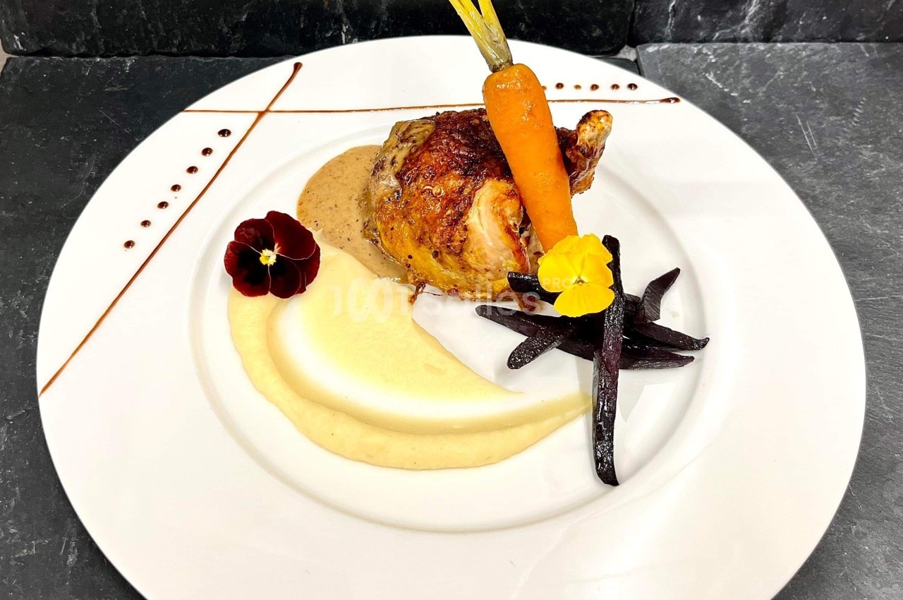 Assiette gastronomique avec volaille rôtie, purée, carotte, légumes noirs et fleurs comestibles sur fond d'ardoise.