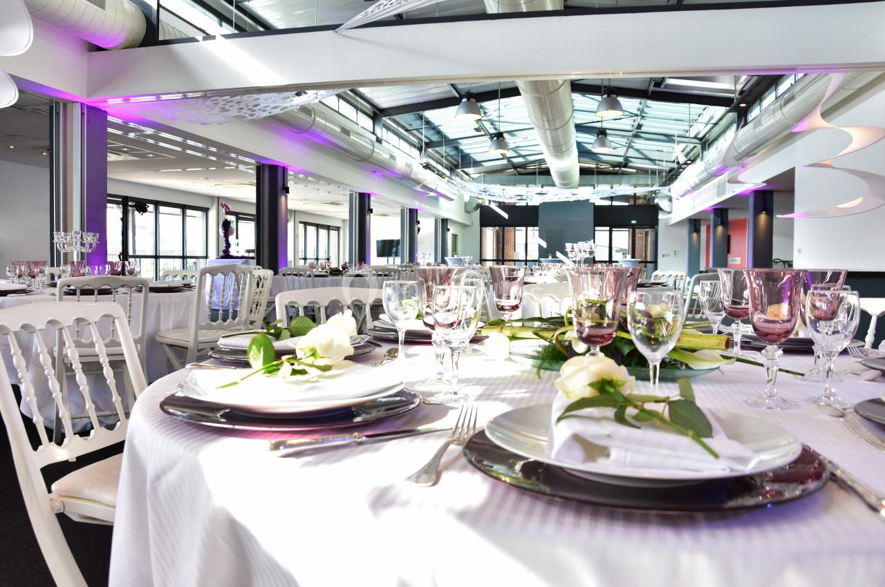 Salle de réception lumineuse avec tables élégamment dressées, décorées de fleurs blanches et vaisselle raffinée.