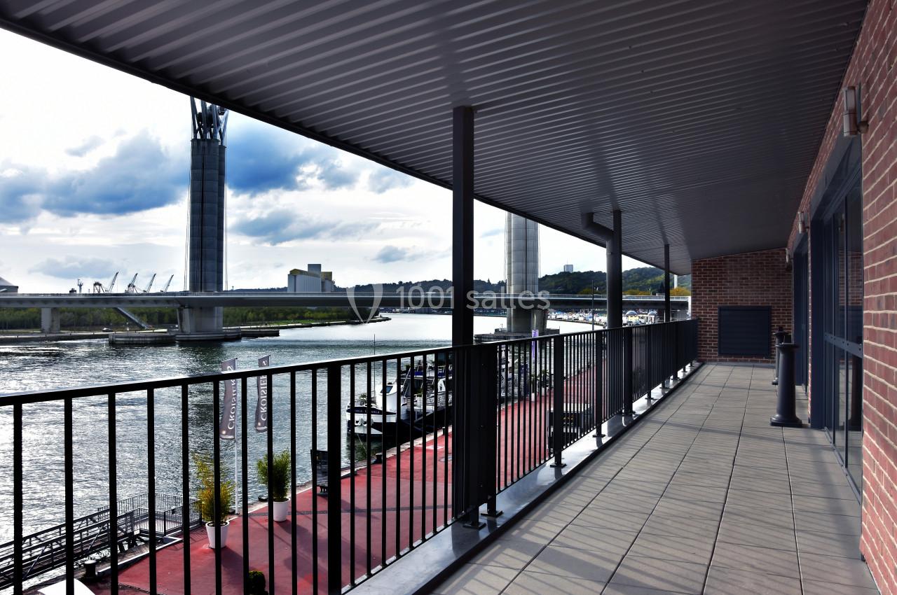 Balcon couvert avec vue sur une rivière, un pont moderne et des quais bordés de bâtiments et de végétation.