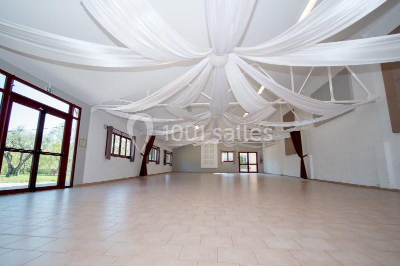 Grande salle lumineuse avec un sol en carrelage beige, des murs blancs et un plafond décoré de voilages suspendus.